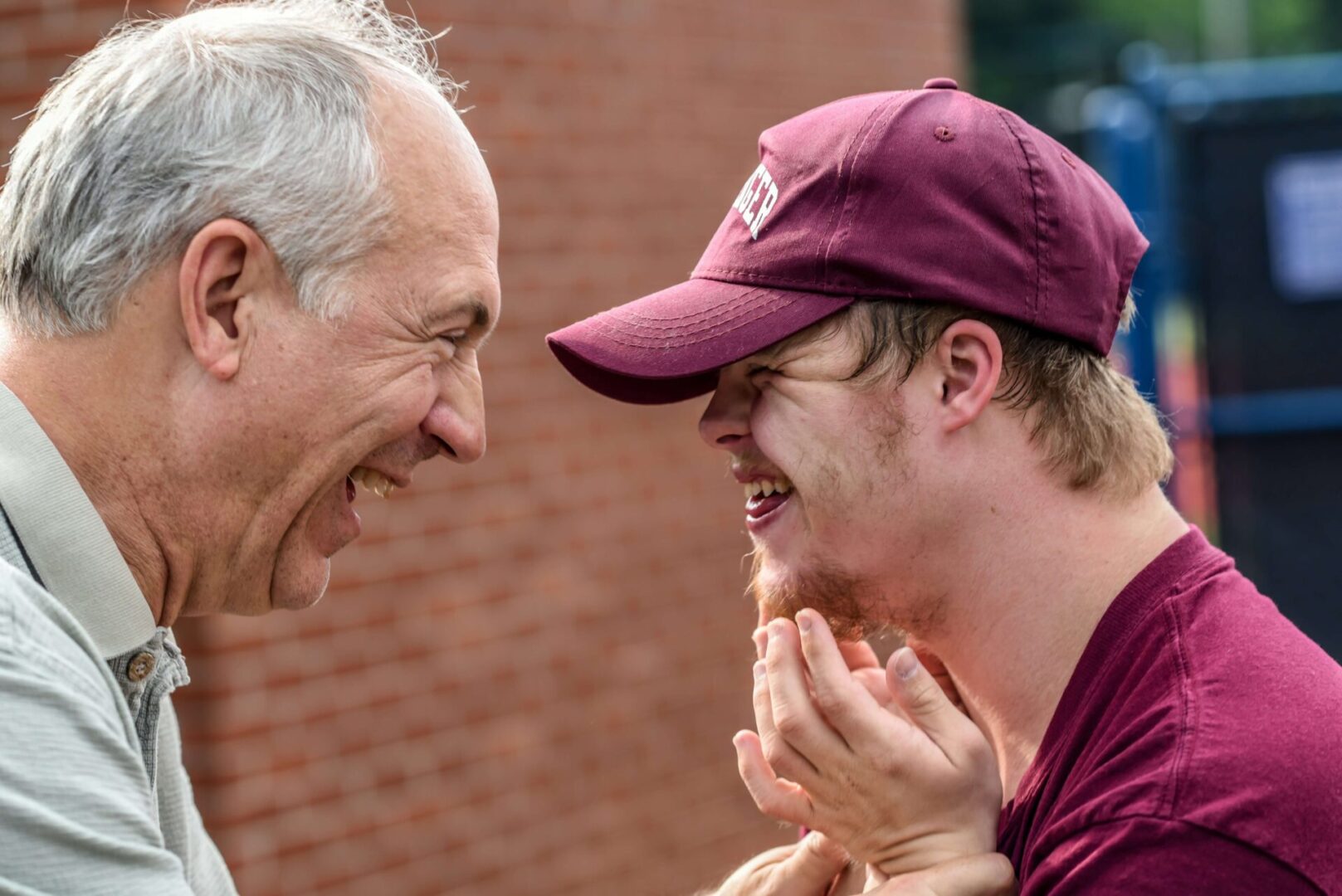 Two men laughing together while one of them is wearing a hat.